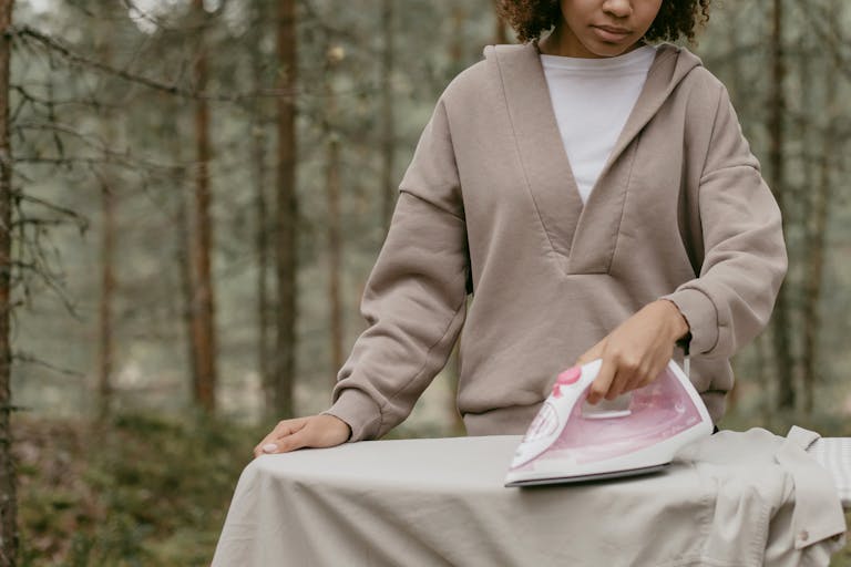 A woman irons a shirt on a board in the tranquil setting of a forest.